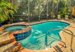 An indoor swimming pool with a hot tub, surrounded by glass walls and a brick deck.