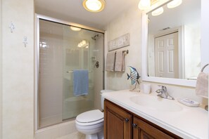 A bathroom with a glass-enclosed shower, a white toilet, a wooden vanity with a sink, and a mirror above the vanity.