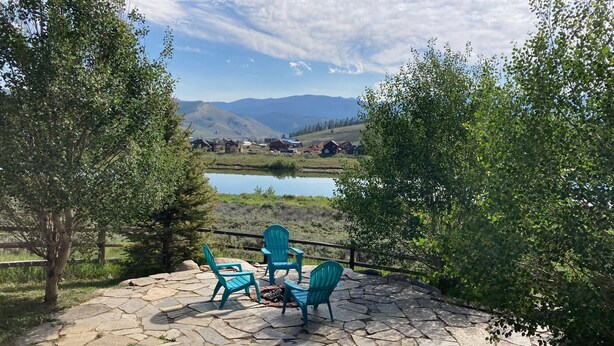 Un patio de piedra con mobiliario exterior, vista a un lago y casas al fondo.