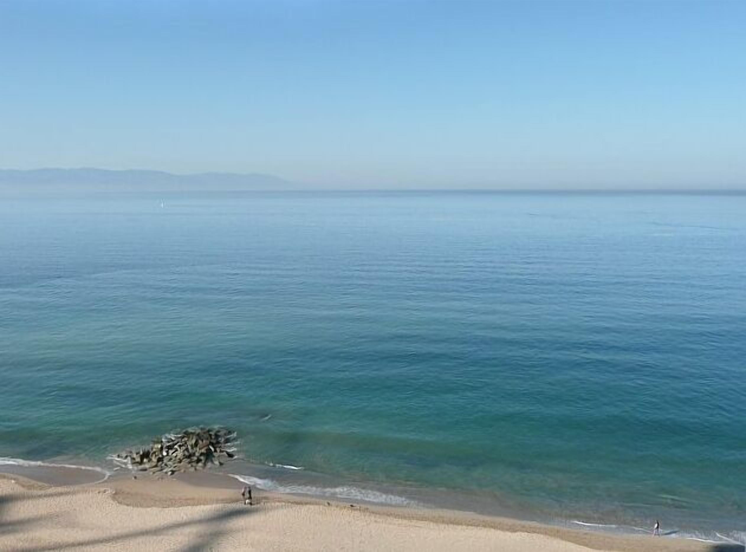 A beach with clear water and distant mountains.
