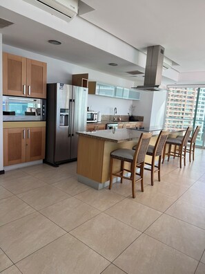 A modern kitchen with a central island, wooden cabinets, stainless steel appliances, and a view of high-rise buildings.