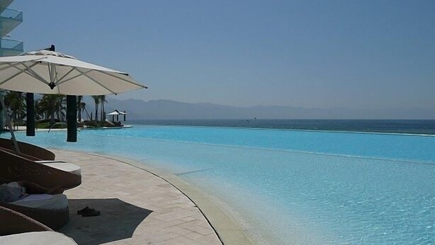 A pool area with lounge chairs and umbrellas, overlooking a clear blue ocean. - Peninsula Vallarta-Luxurious/Huge Oceanfront Condo w/ Spectacular View (Puerto Vallarta)