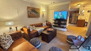 Un salon avec un canapé marron, une table basse et un téléviseur. Il y a un tableau au mur et une lampe sur la table d’appoint.