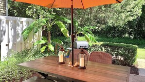Une terrasse extérieure avec une table en bois, deux lanternes et un parasol orange.