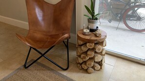 Un fauteuil en cuir marron avec des pieds en métal, un tabouret en bois fait de rondins, une plante en pot et un vélo devant une fenêtre.
