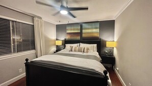 Une chambre à coucher avec un lit, deux lampes de chevet, un ventilateur de plafond et des œuvres d’art accrochées au mur.