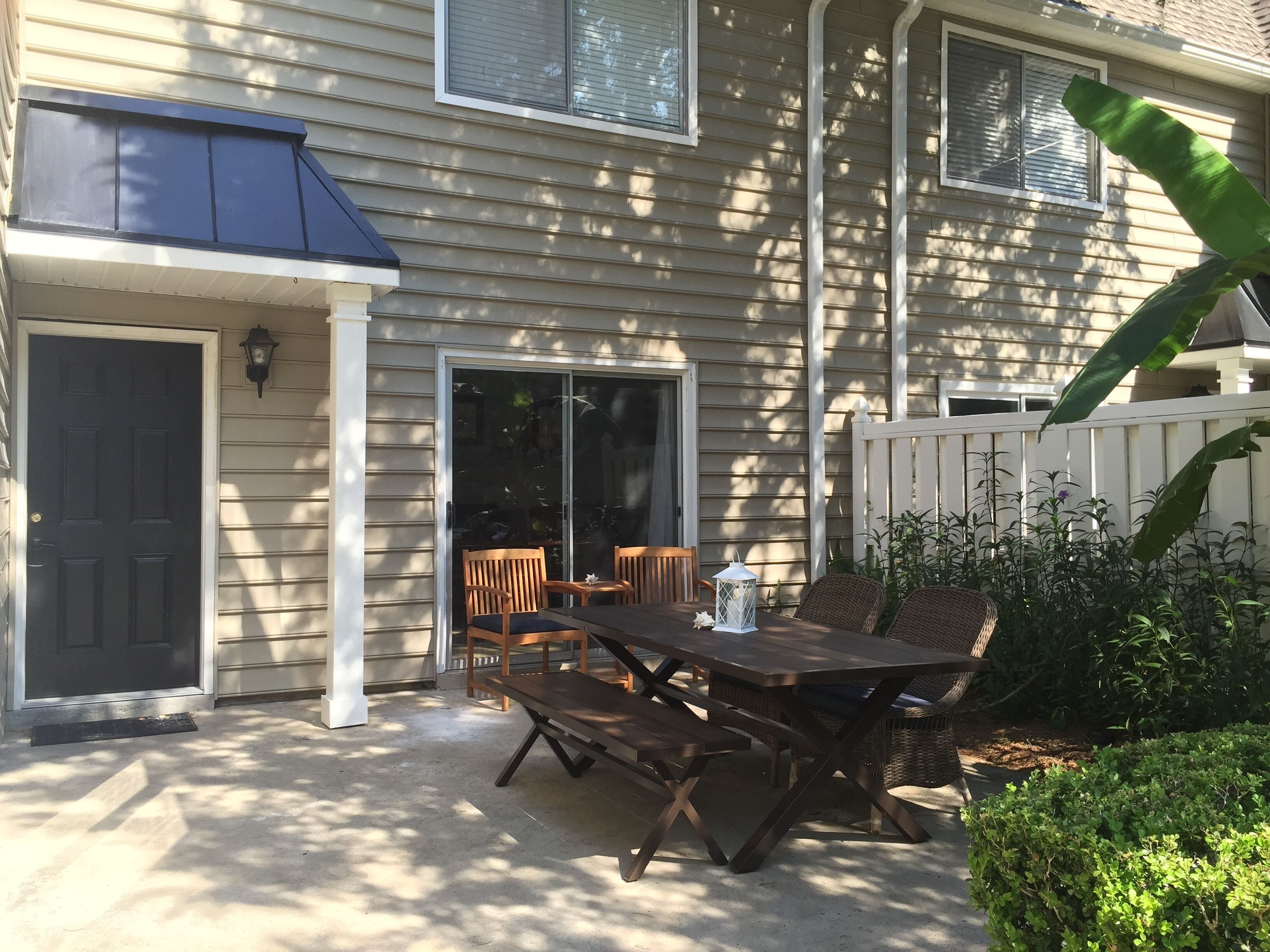 A patio with a table and chairs, a sliding glass door, and a white fence.