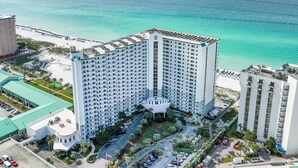 A high-rise hotel with a central courtyard, adjacent to a beach with a clear view of the ocean.