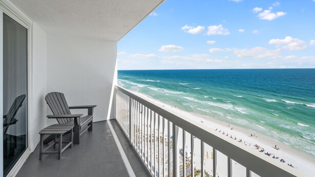 A balcony with two Adirondack chairs, a white railing, and a view of the ocean and beach.