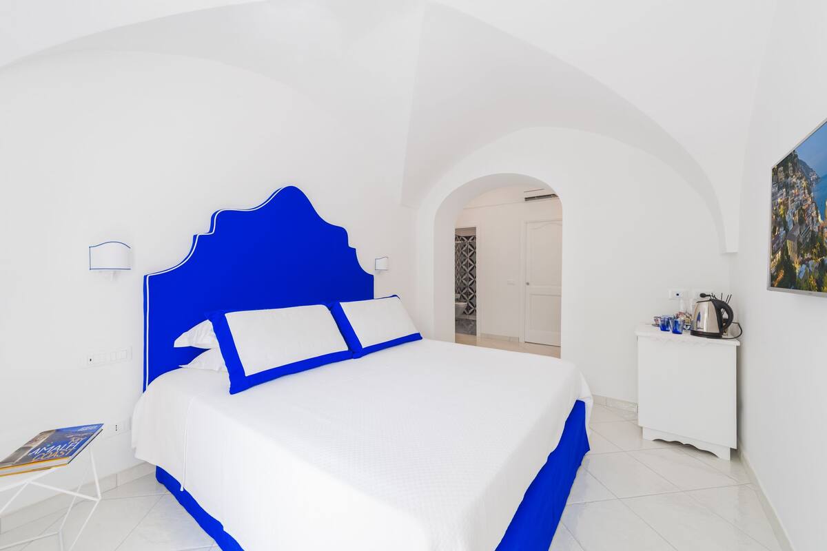 A modern bedroom with a large bed, white walls, and a blue accent wall.