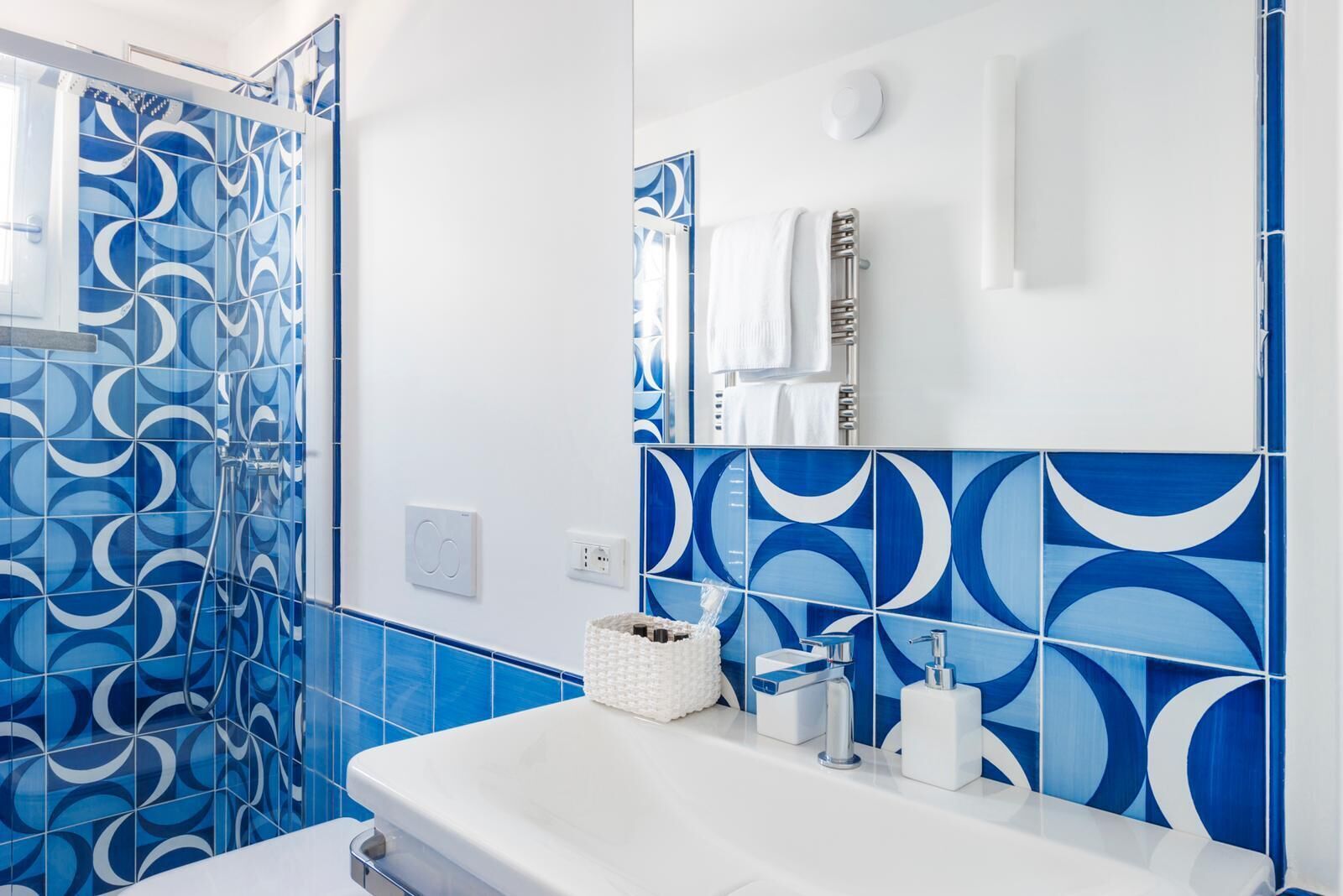 A modern bathroom with blue and white patterned tiles, a white sink, and a mirror above it.