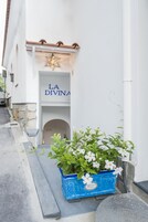 Un estrecho callejón con la entrada de un edificio que dice "LA DIVINA" y una maceta azul con flores blancas en el frente.