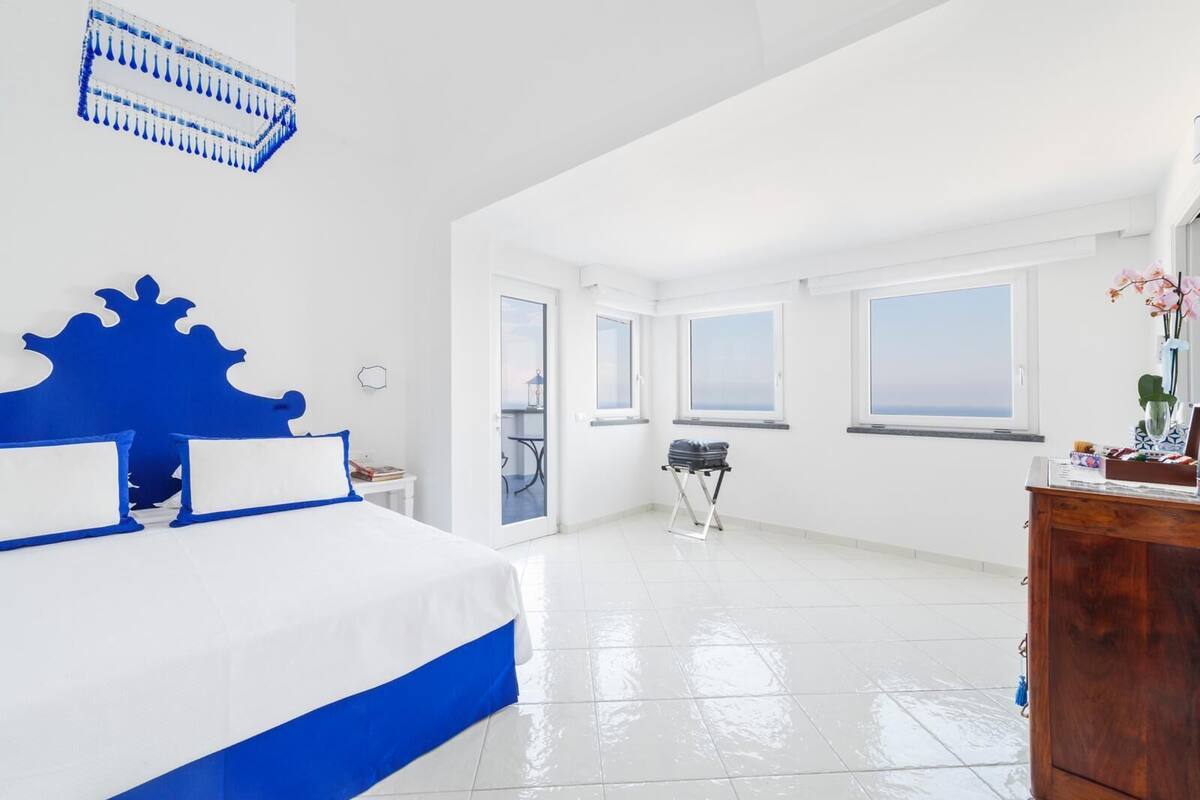 A spacious hotel room with a large bed, a wooden dresser, and a balcony with a view.