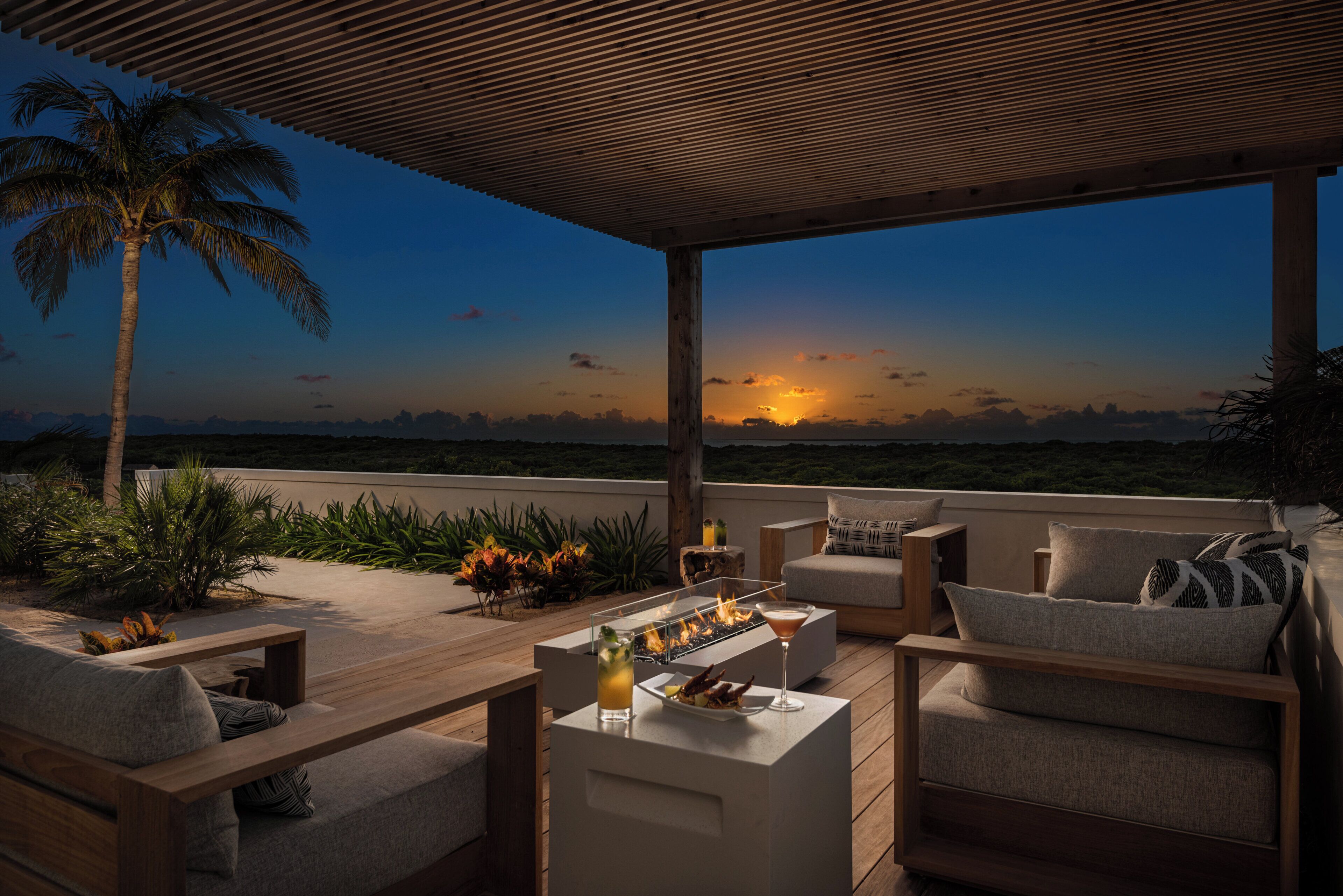 Une terrasse extérieure avec une plateforme en bois, un espace salon et une vue sur le coucher de soleil.