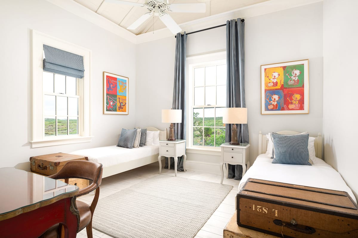 A bedroom with a bed, bedside tables, a desk, a chair, a suitcase, and artwork on the walls.
