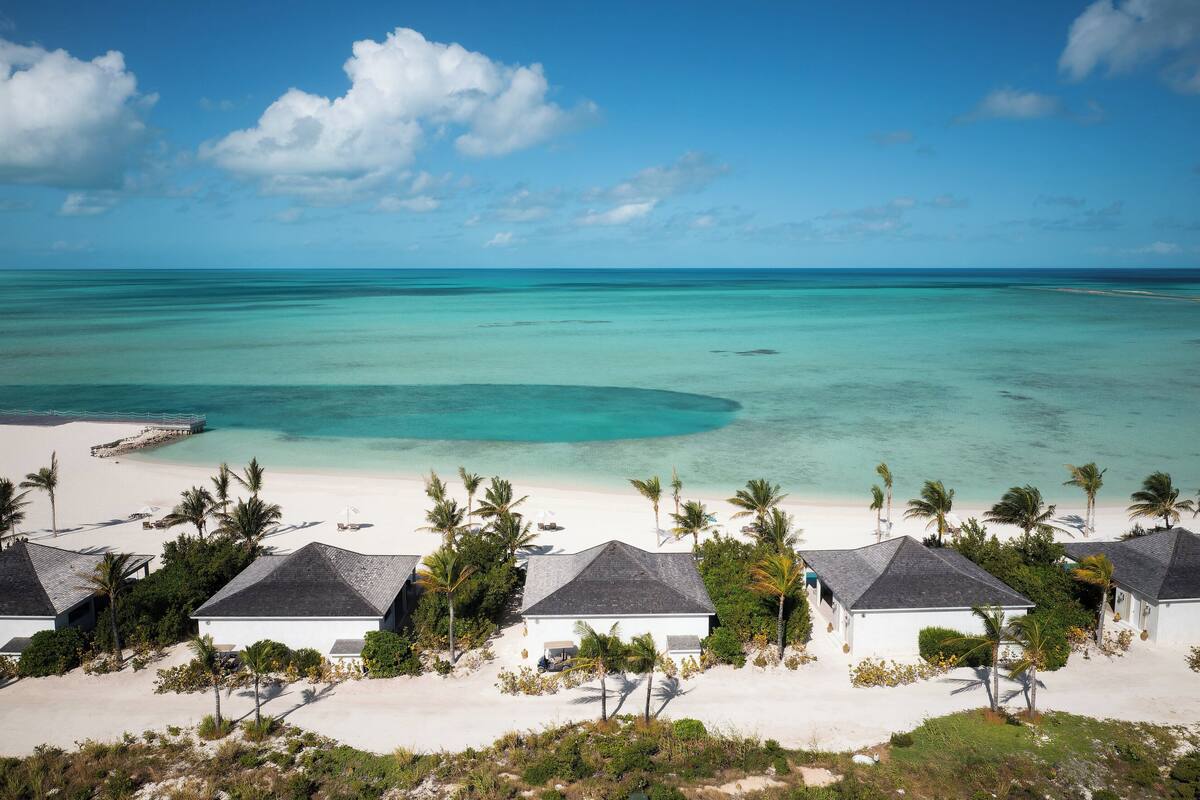 A beach resort with white buildings, palm trees, and a clear blue sea.