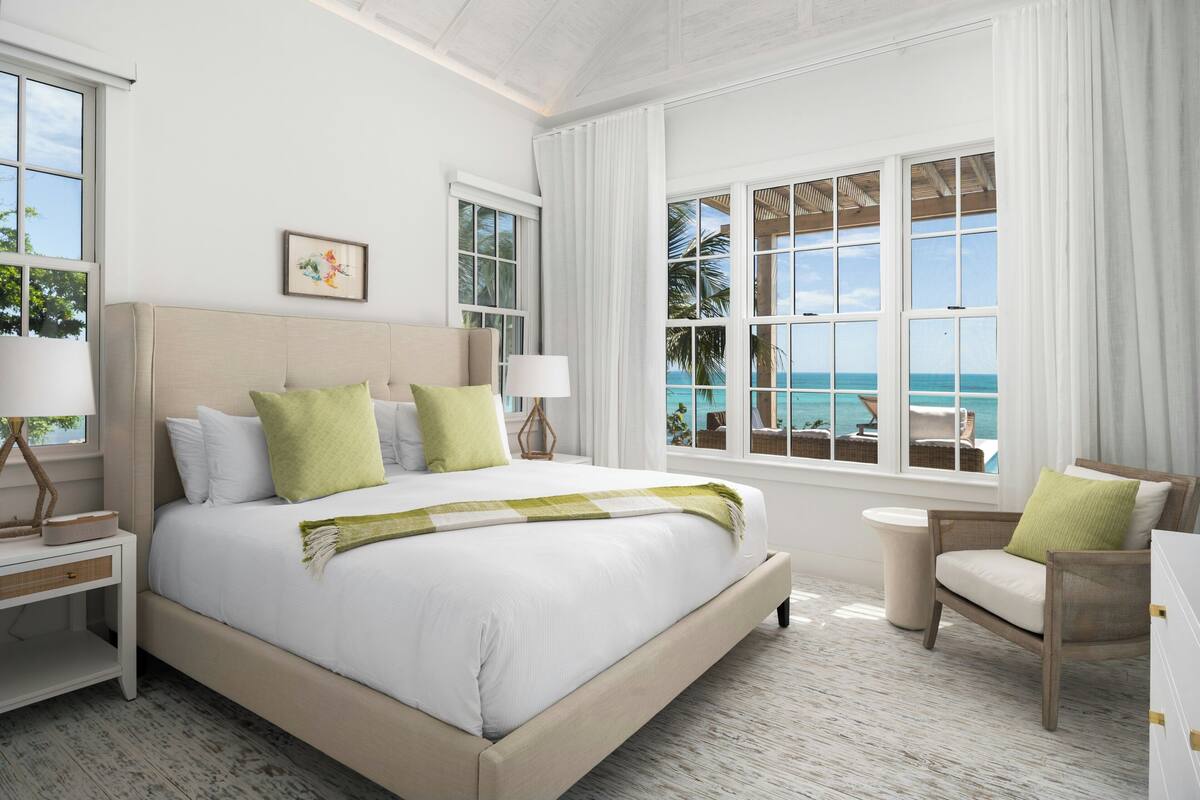 A bedroom with a large bed, a chair, a nightstand, and a view of the ocean.