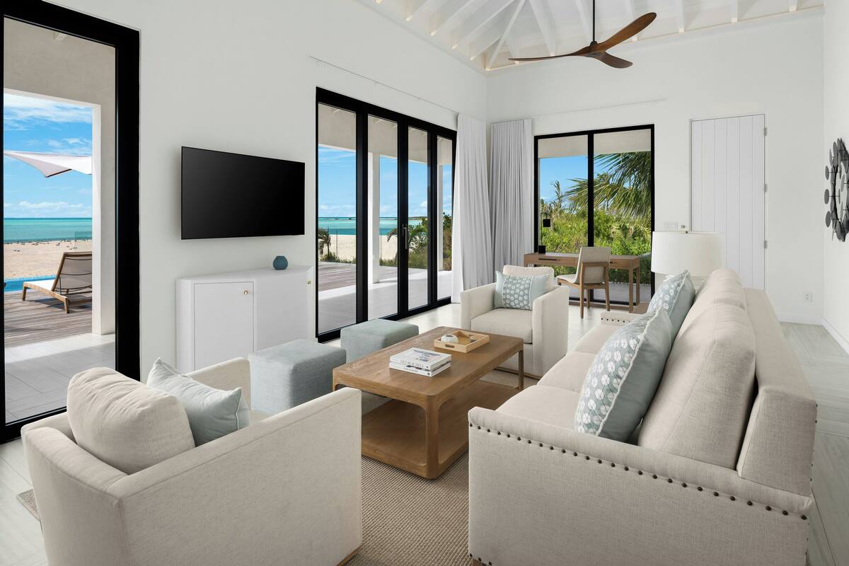 A modern living room with a sofa, coffee table, and TV, overlooking a beach.