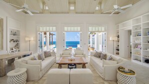 A spacious living room with a large wooden coffee table, white sofas, and a view of the ocean. - Ambergris Cay Private Island - All-Inclusive (Big Ambergris Cay)
