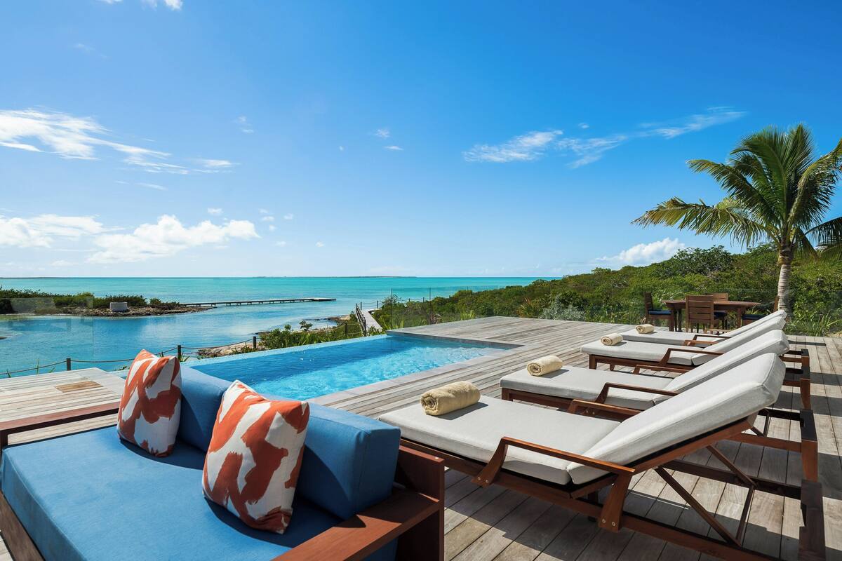 A poolside area with lounge chairs, a wooden deck, and a view of the ocean.