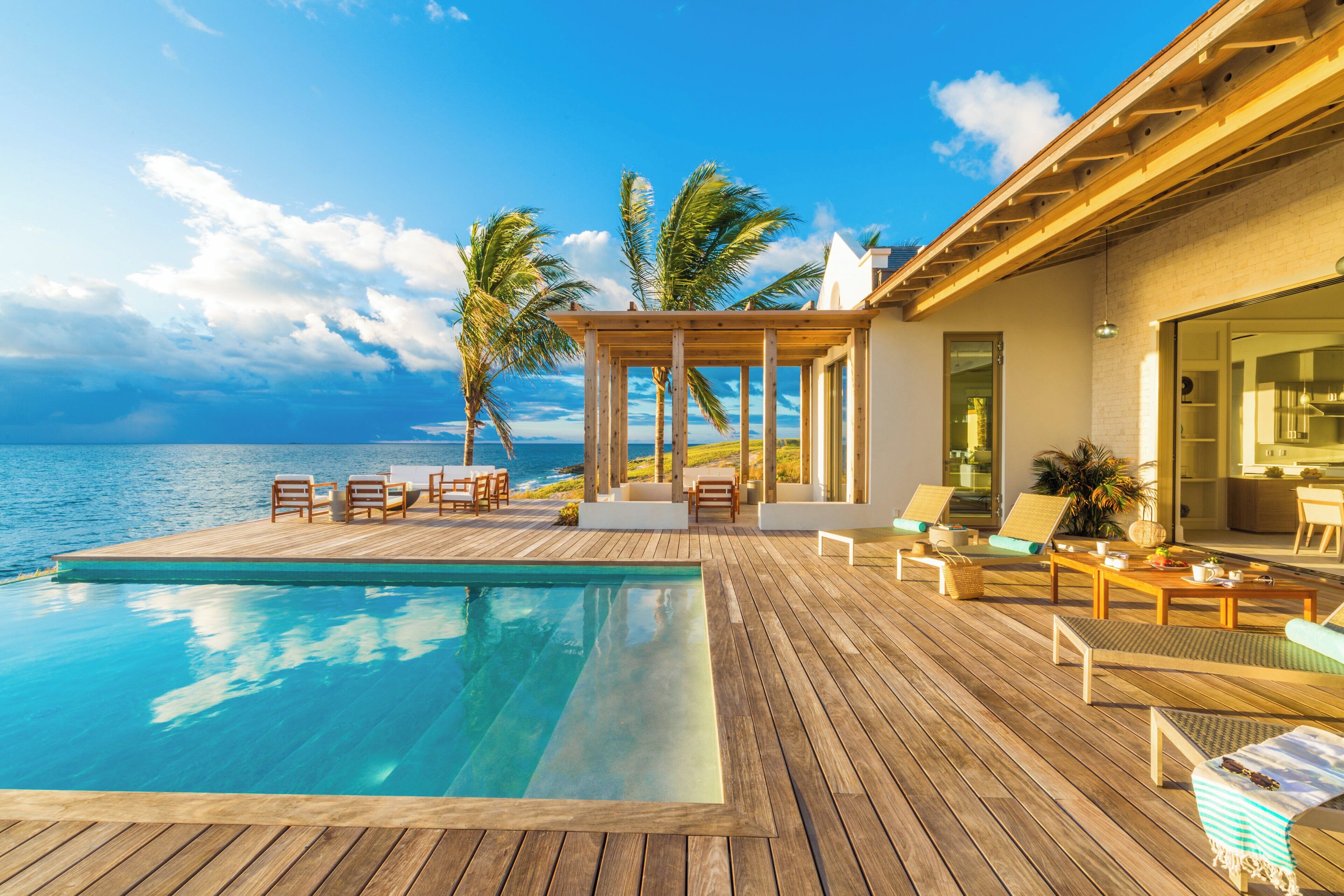 Une terrasse en bois avec une piscine, un espace salon extérieur et une vue sur l’océan.