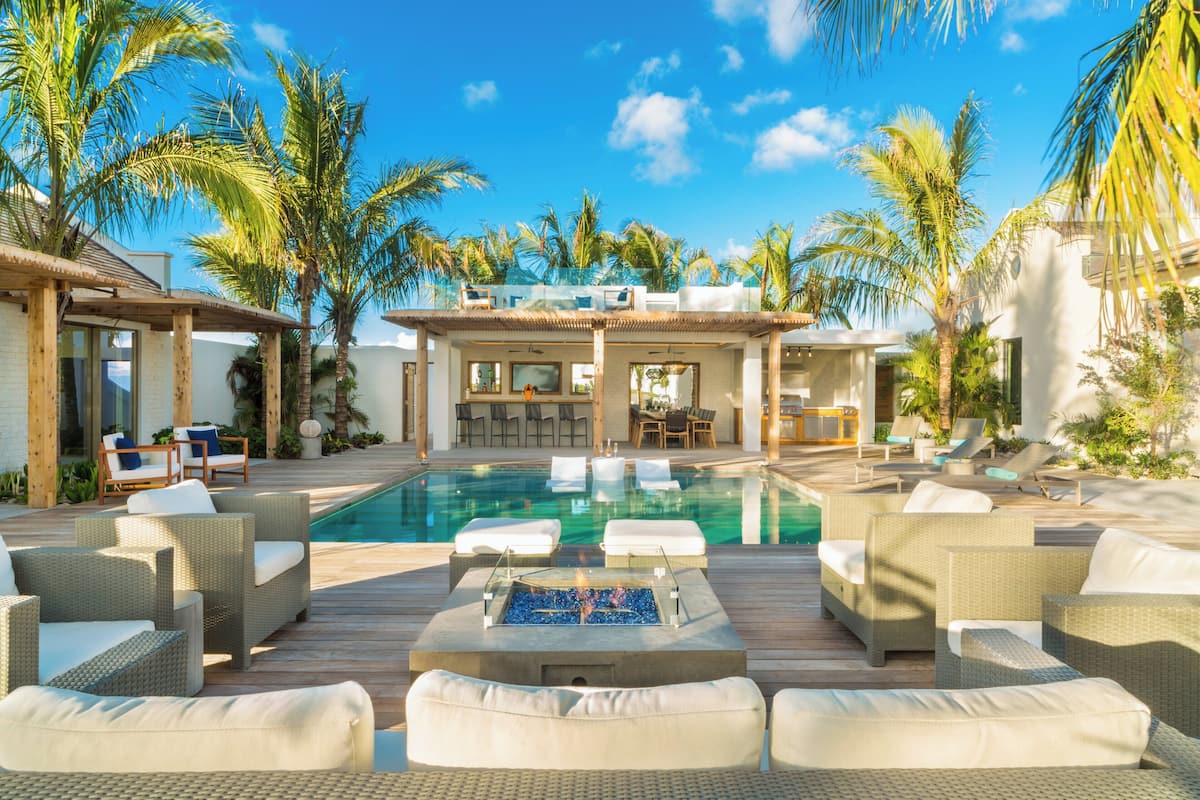 A pool area with lounge chairs, a fire pit, and a bar area with seating.