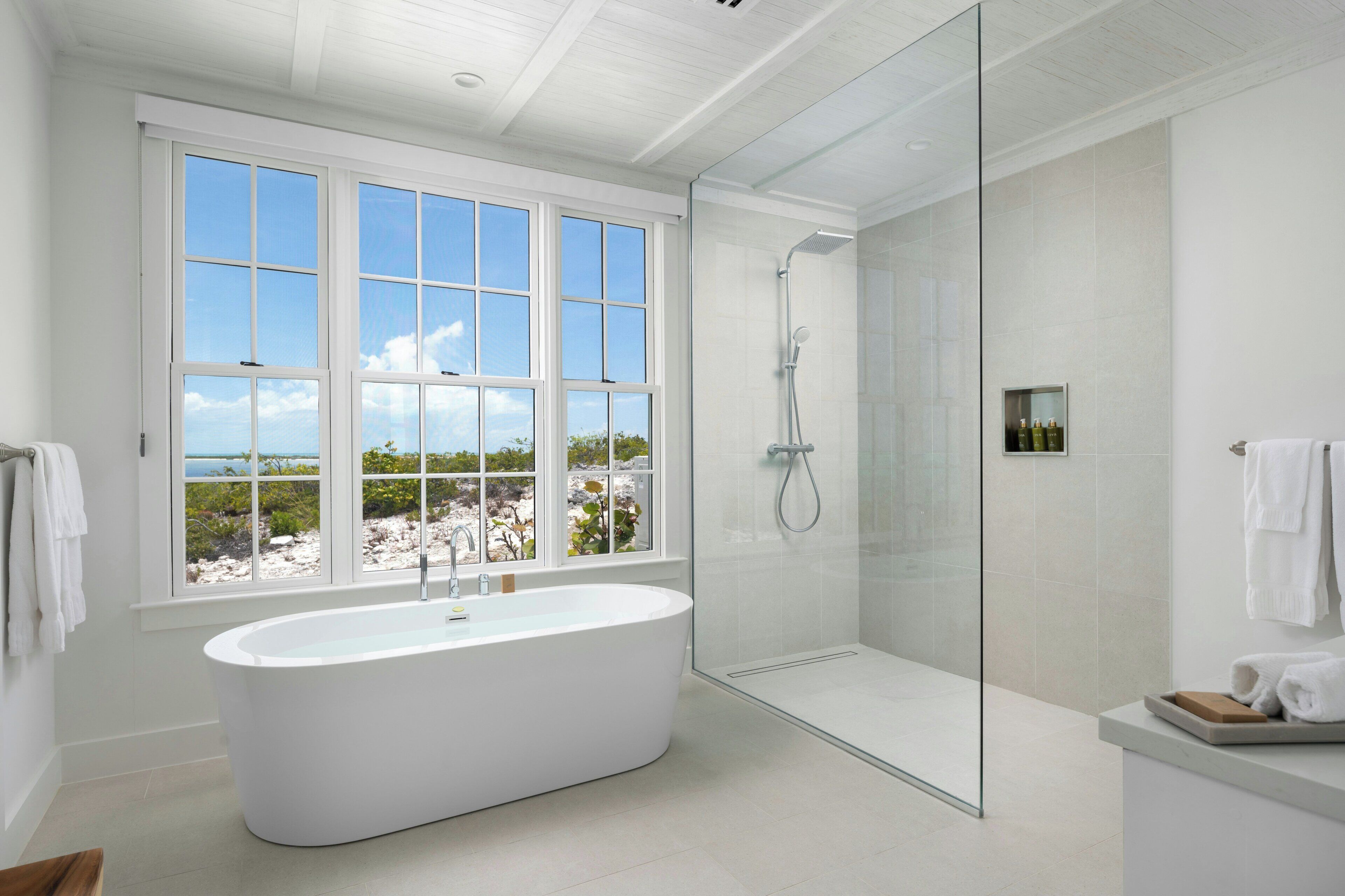 Une salle de bain moderne avec une baignoire sur pieds, une douche à parois de verre et une grande fenêtre donnant sur l’extérieur.