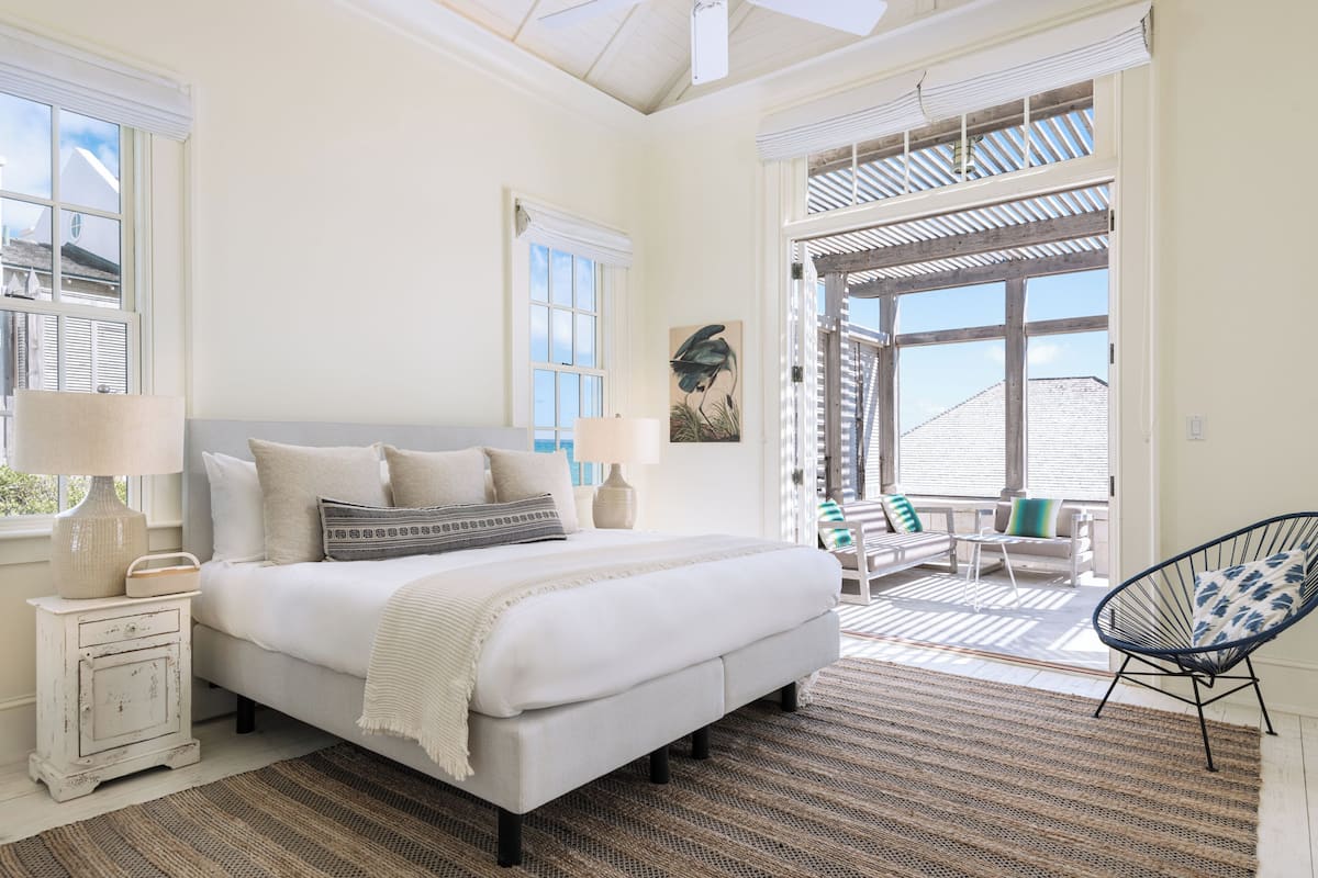 A bedroom with a bed, bedside tables, a window, and a view of the outside.