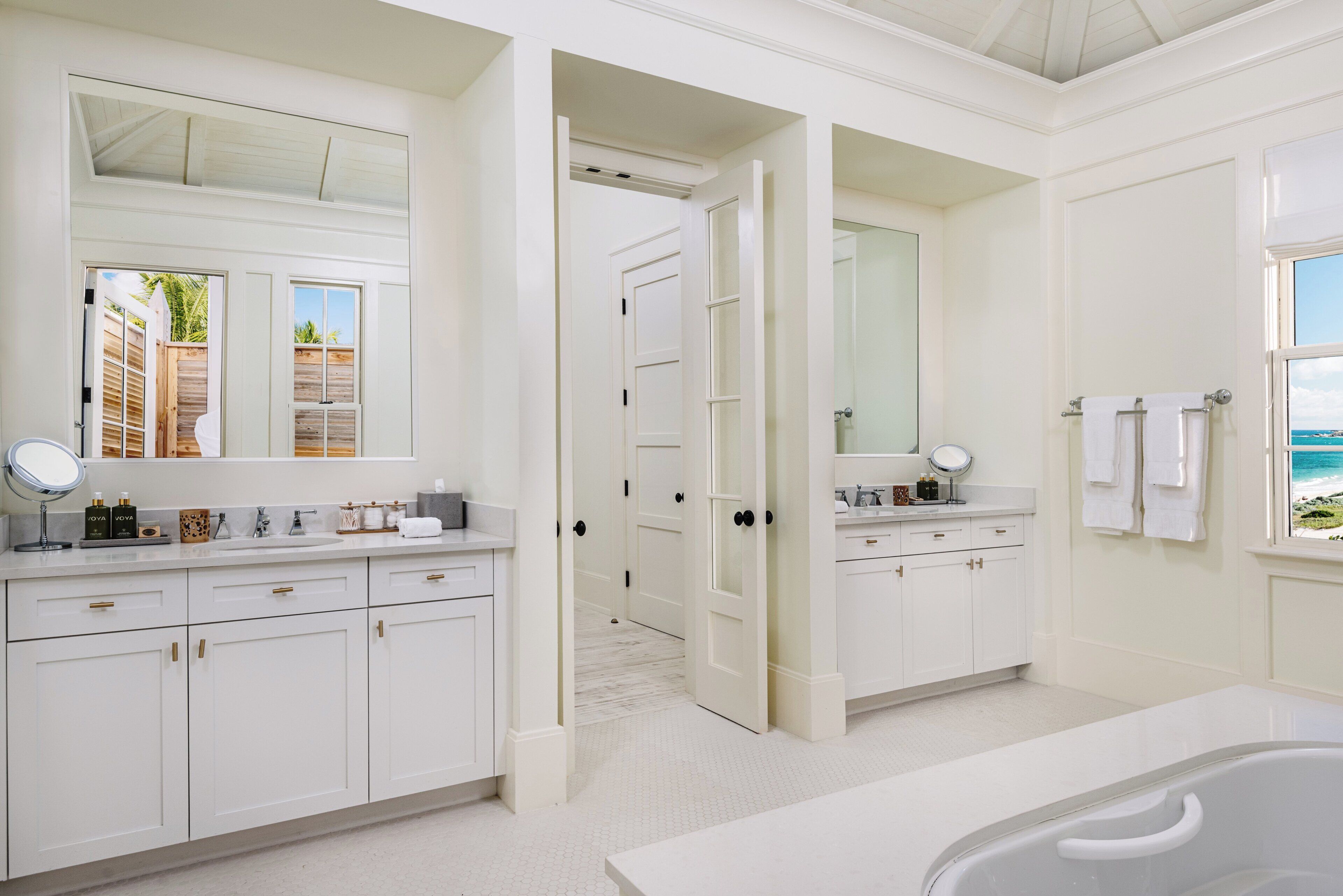A bathroom with white cabinetry, a large mirror, and a bathtub.