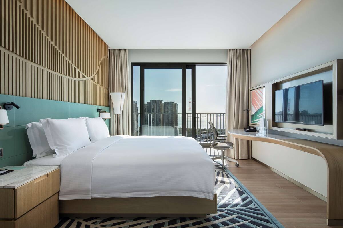 A modern hotel room with a large bed, a TV, and a balcony with a city view.