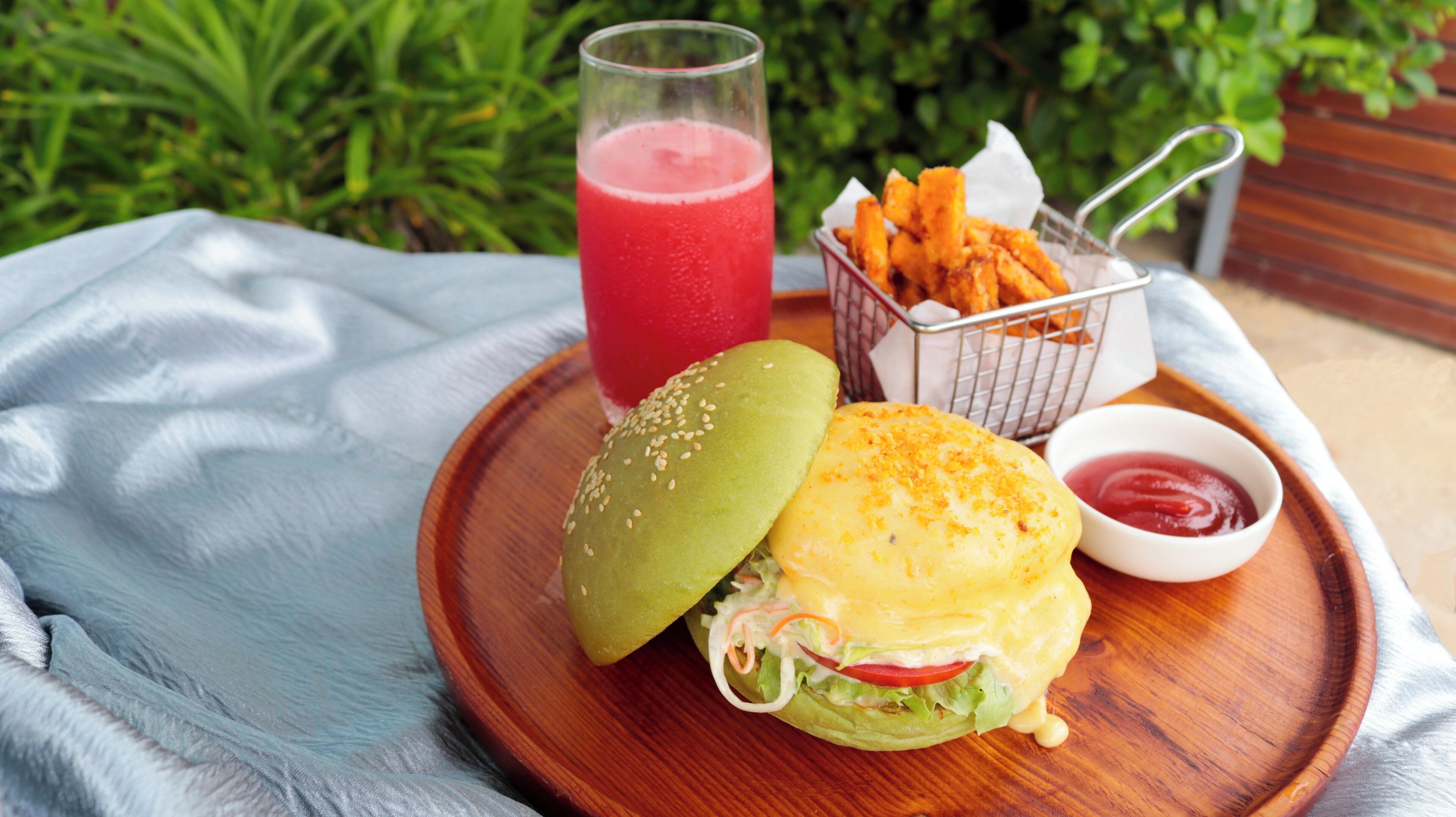 A meal with a burger, a drink, and a side dish on a wooden tray.