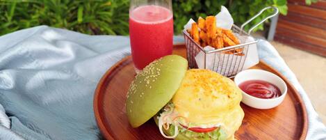 A meal with a burger, a drink, and a side dish on a wooden tray.