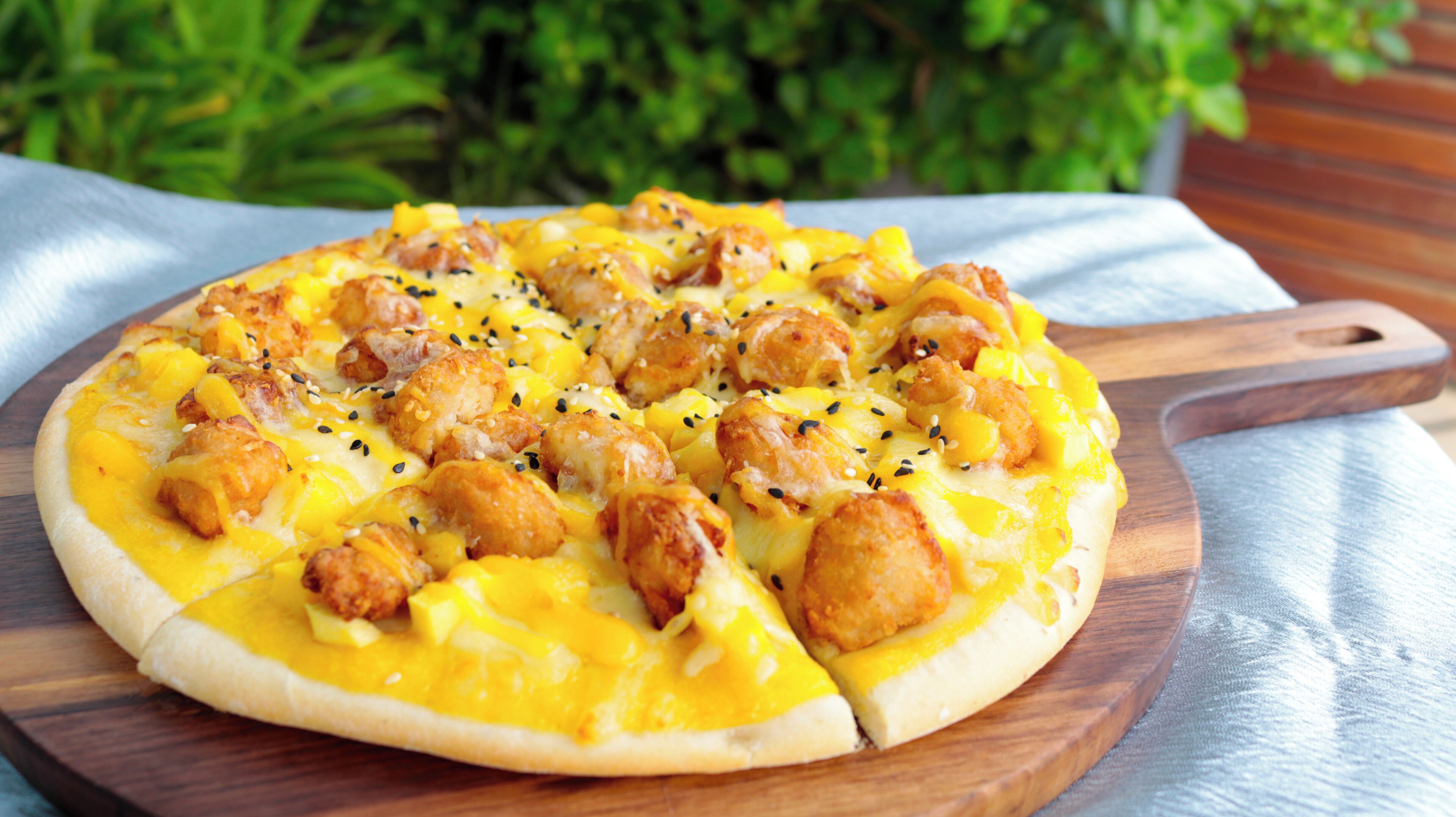 En pizza på en træbræt med håndtag, placeret på et bord dækket med et hvidt stof.