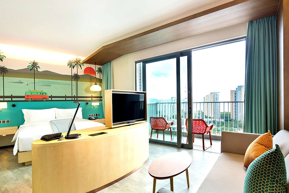 A hotel room with a bed, desk, TV, and a balcony with chairs and a sofa.