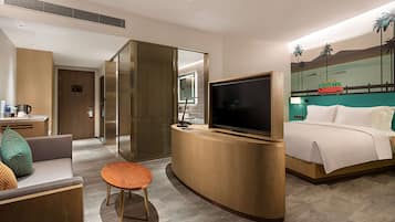 Habitación de hotel con cama, televisor, escritorio con una computadora portátil, cafetera y un mural en la pared.