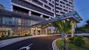 A modern hotel entrance with a covered walkway, glass railings, and a landscaped area with palm trees. - Hilton Garden Inn Sanya (Sanya)