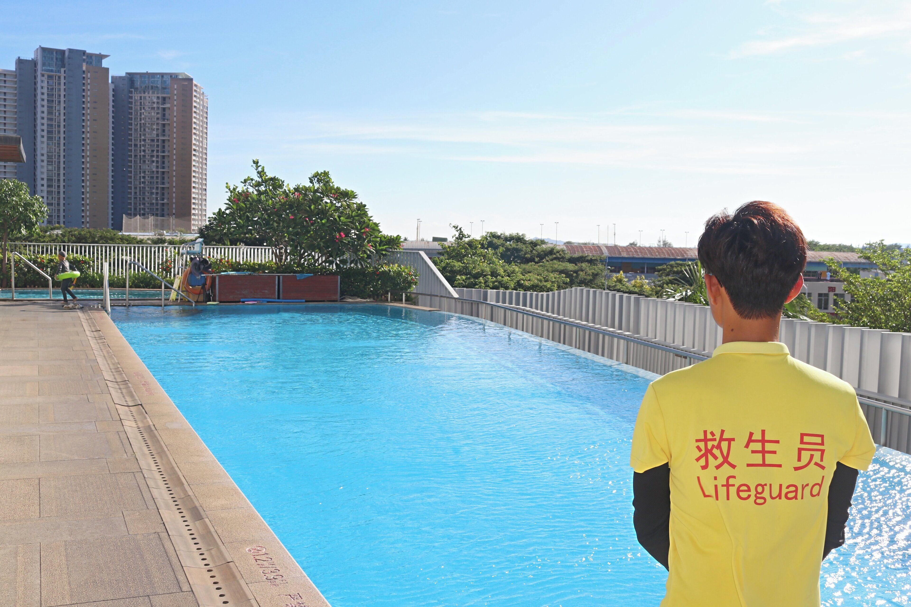 Un sauveteur est en poste près d'une piscine, avec une vue sur la ville en arrière-plan.