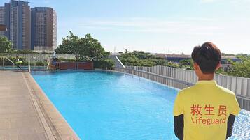A lifeguard standing by a pool with a cityscape in the background.