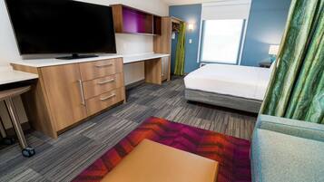 A hotel room with a bed, a desk with a TV, a wardrobe, and a colorful rug.