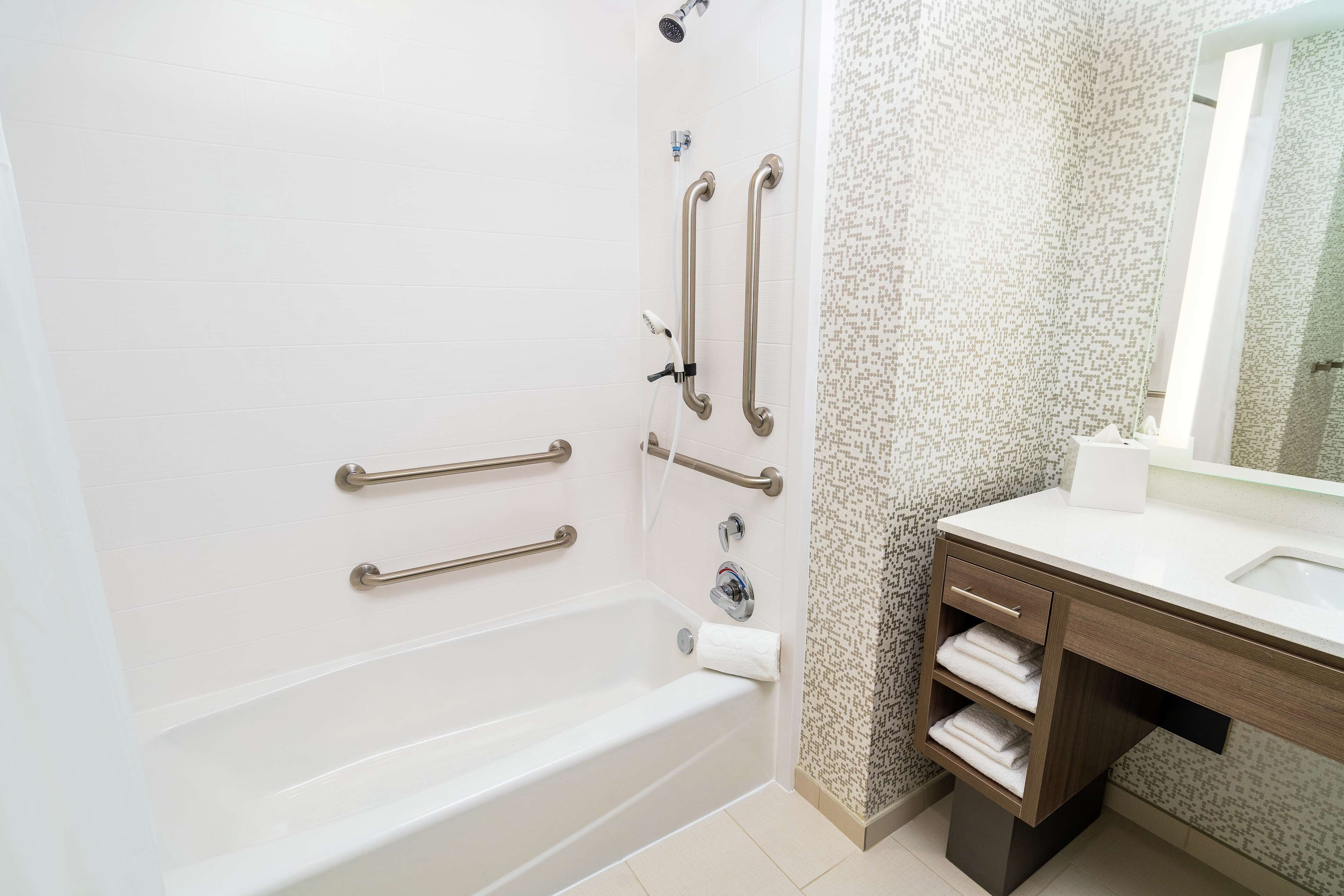 A modern bathroom with a bathtub, grab bars, a sink, and a vanity with towels.
