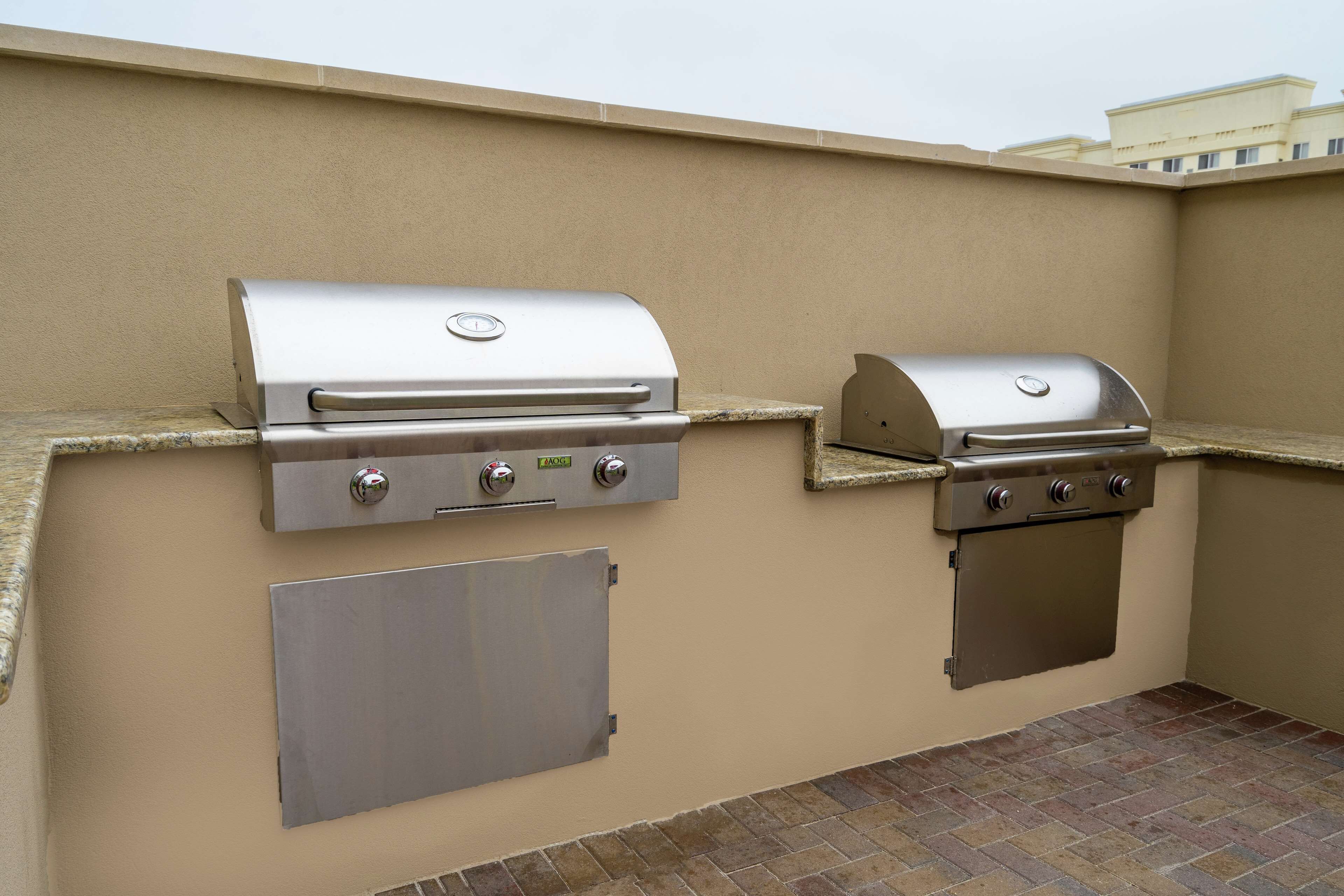 An outdoor barbecue area with two stainless steel grills, a built-in cooler, and a brick floor.