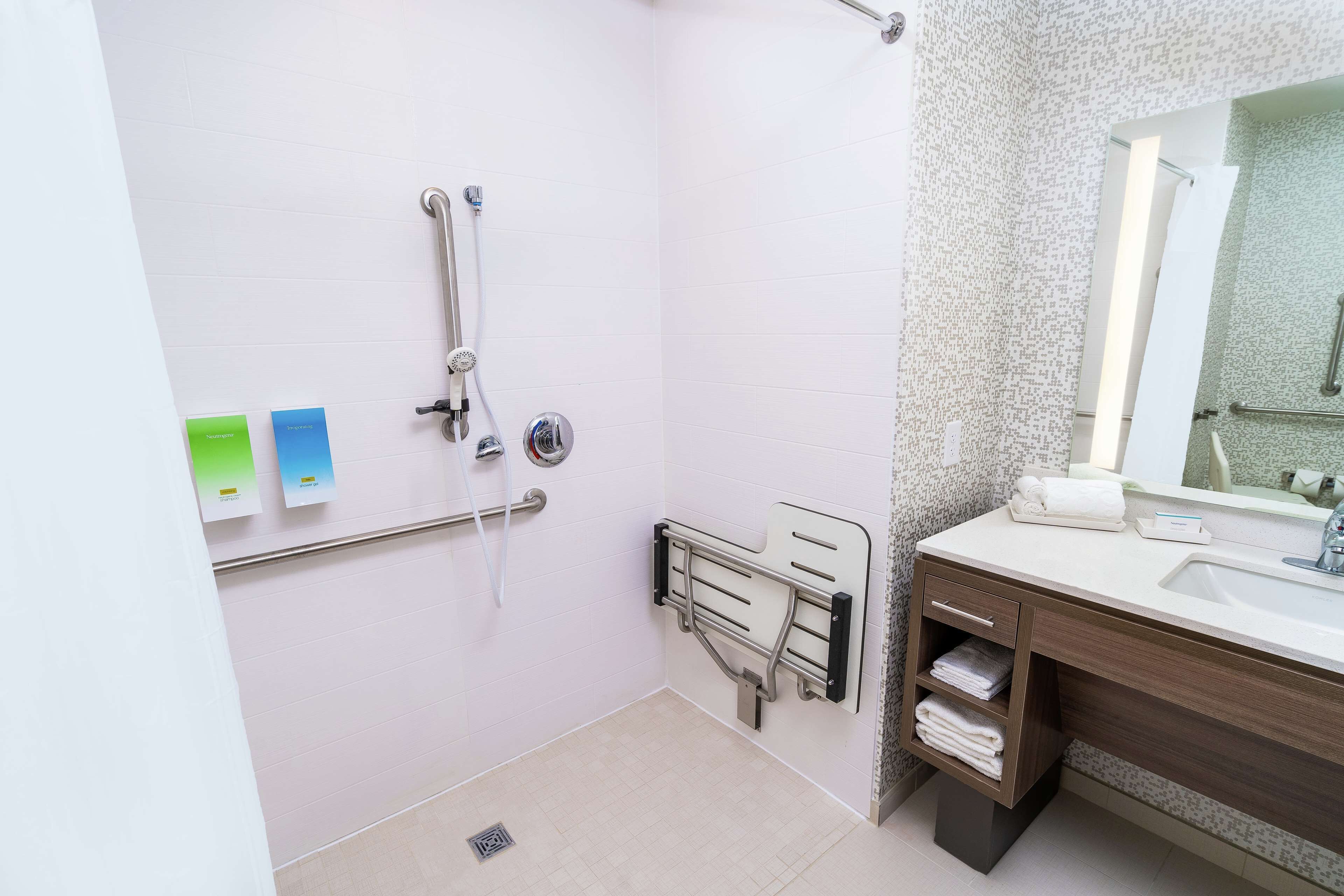 A bathroom with a shower, grab bars, a sink, and a towel rack.