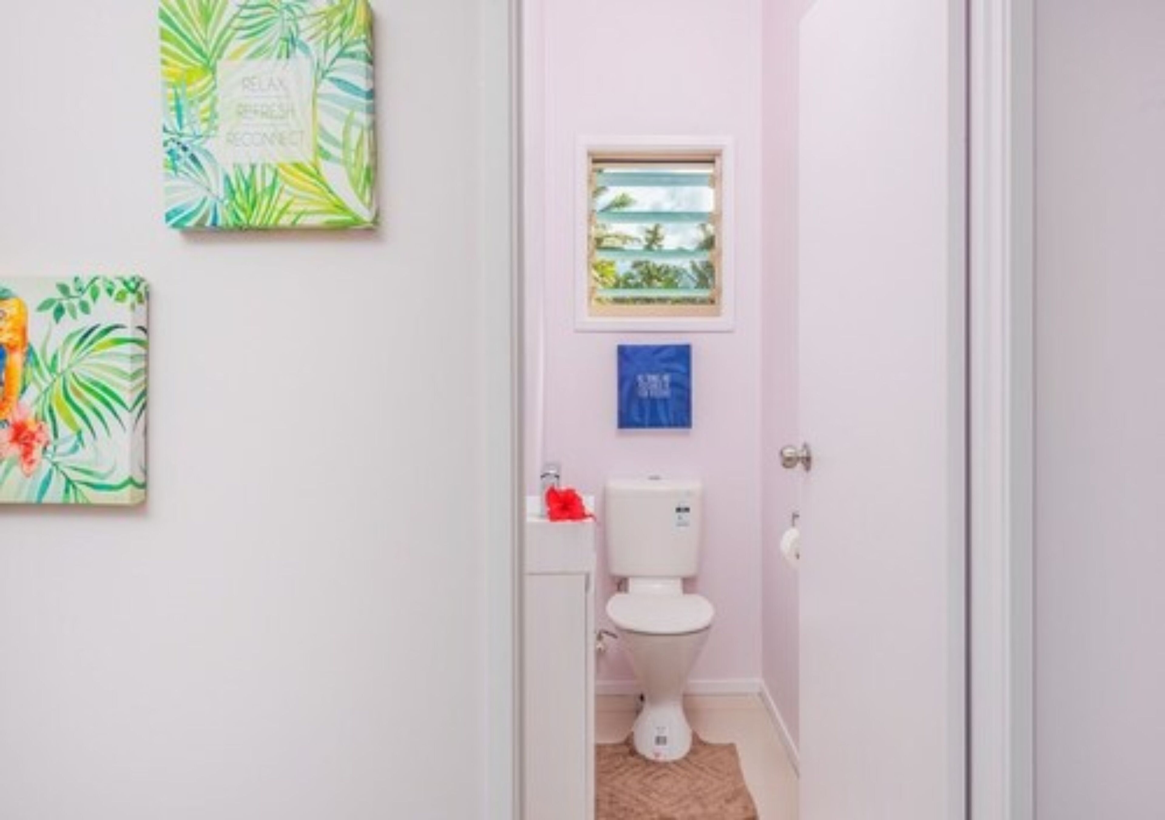 Un baño pequeño con un inodoro, una ventana y dos obras de arte colgadas en la pared.