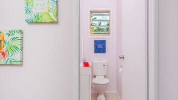 Un baño pequeño con un inodoro, una ventana y dos obras de arte colgadas en la pared.