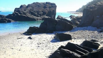 Ein felsiger Strand mit großen Steinen und klarem, blauem Wasser.