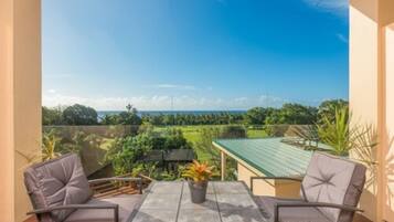 A balcony with two chairs and a table, overlooking a green landscape and a body of water.