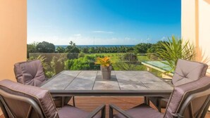 A patio with a table and chairs, a potted plant, and a view of a green landscape.