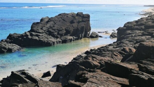 A rocky shoreline with clear blue water and a sandy beach.