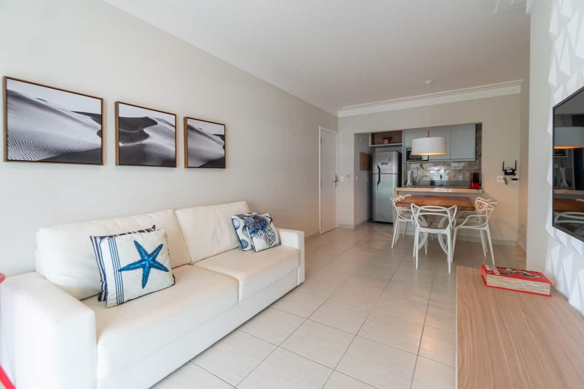 A modern living room with a white sofa, a dining table, and a kitchen in the background.