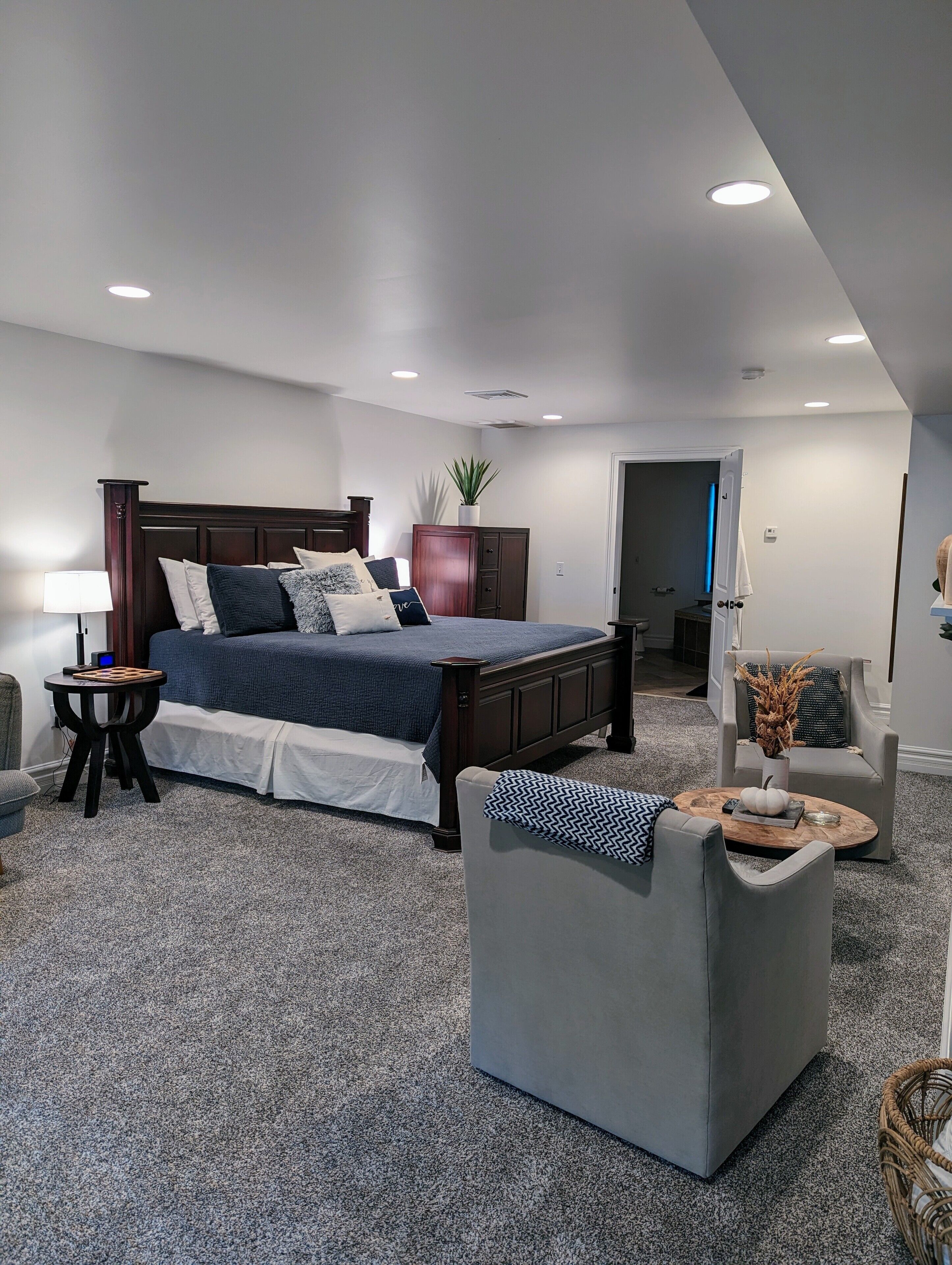 A bedroom with a large bed, a bedside table, a chair, and a small table with a lamp.